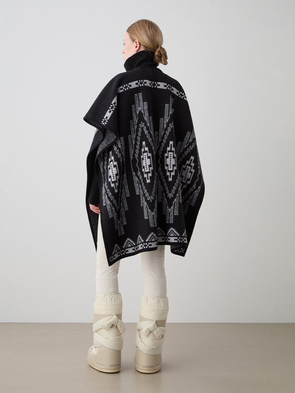 We Norwegians_FW25_Womens | Model is wearing the Pioneer poncho | Black in color with a jacquard pattern | Made with boiled merino wool | Back view