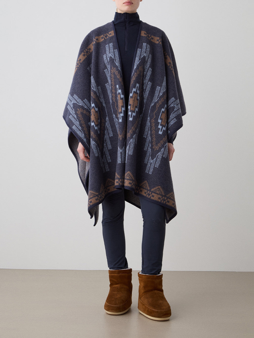 We Norwegians_FW25_Womens | Model is wearing the Pioneer poncho | Navy Blue in color with a jacquard pattern | Made with boiled merino wool | Front view