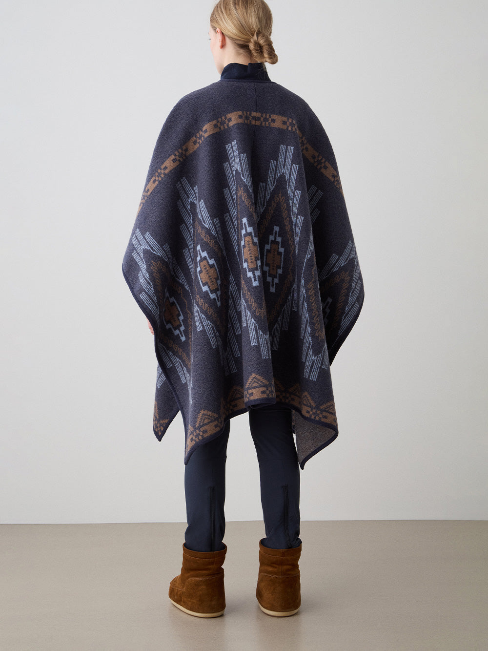 We Norwegians_FW25_Womens | Model is wearing the Pioneer poncho | Navy Blue in color with a jacquard pattern | Made with boiled merino wool | Back view