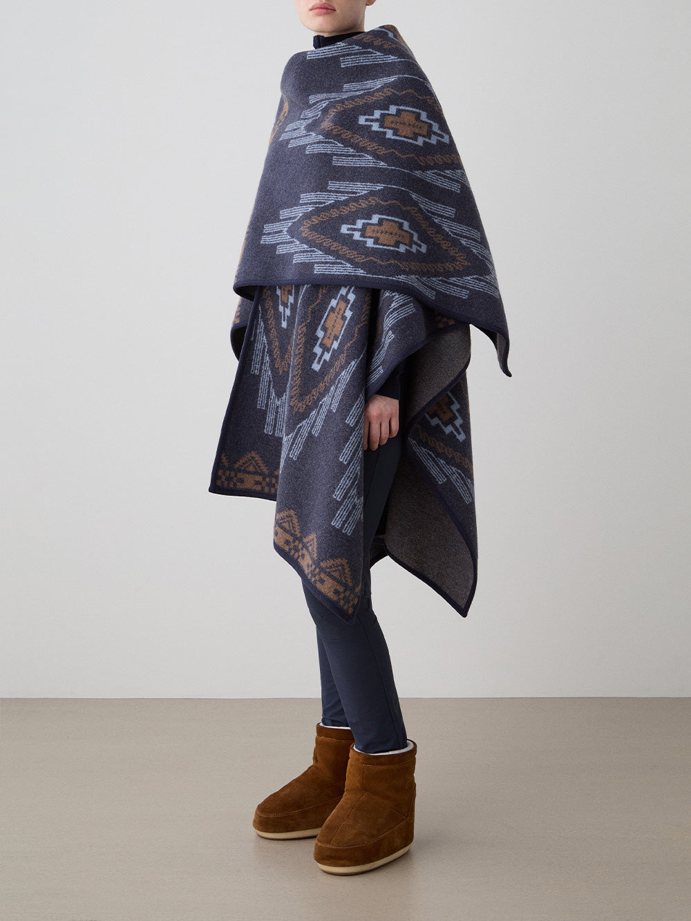 We Norwegians_FW25_Womens | Model is wearing the Pioneer poncho | Navy Blue in color with a jacquard pattern | Made with boiled merino wool | Photograph is showing the fall and drape features of the garment