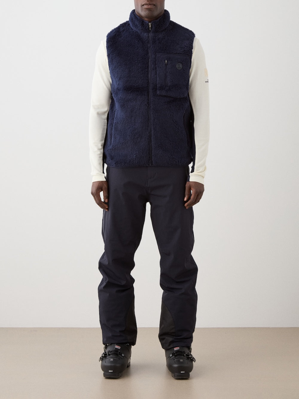 We Norwegians | FW25 | Mens Kebnekaise Vest_Navy blue | Model wearing this fleece vest with front zipper opening, zipped chest pocket and side pockets -over an off-white top - paired with black ski pants | Shot against an off-white background | Front