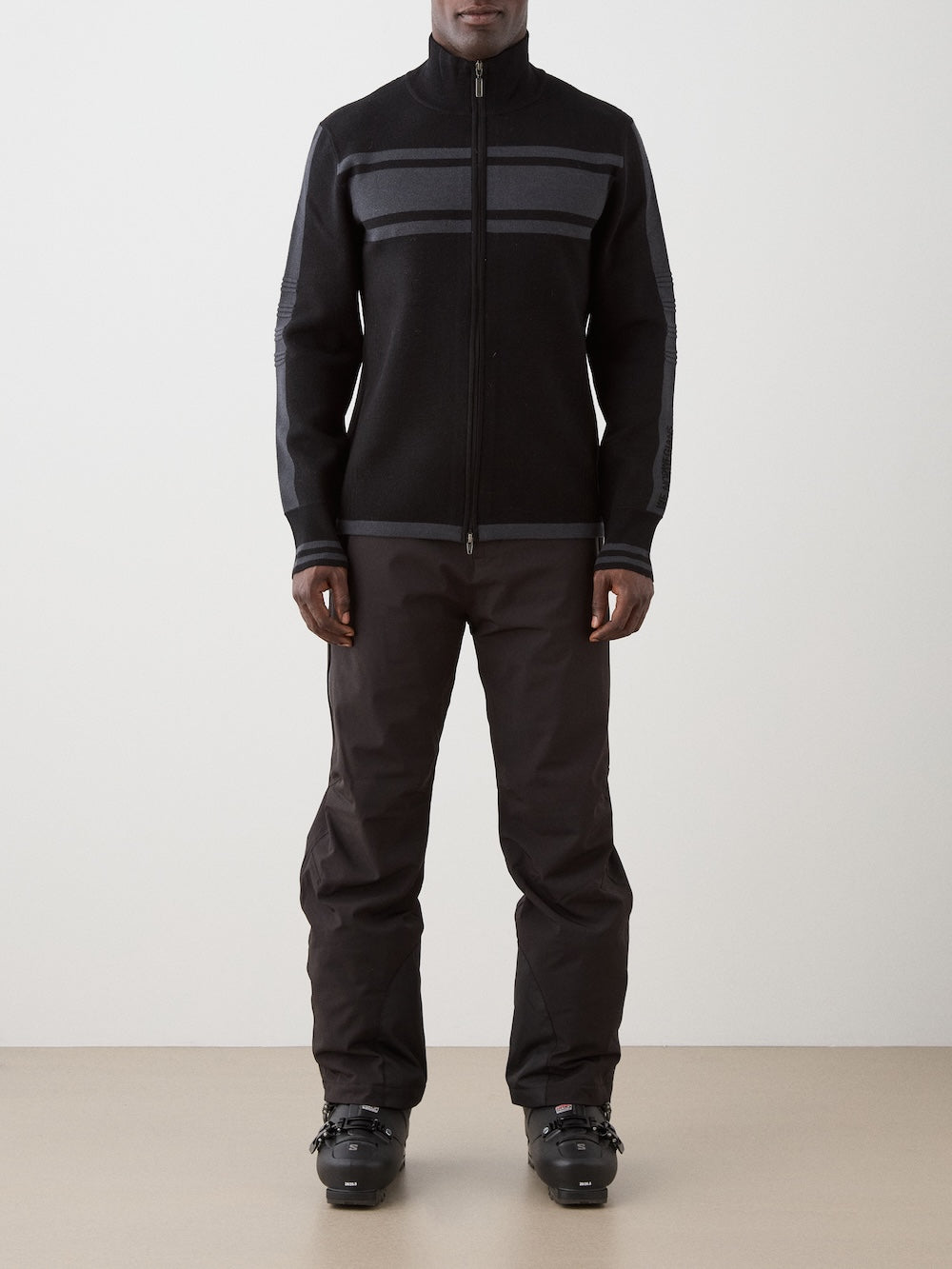 We Norwegians | FW25 | Mens Rocky Full ZipUp_Black | Model wearing this fine knitted sweater with a 2-way front zipper opening, designed in a retro style with subtle color blocks on the chest and sleeves - paired with black ski pants | Shot against an off-white background | Front