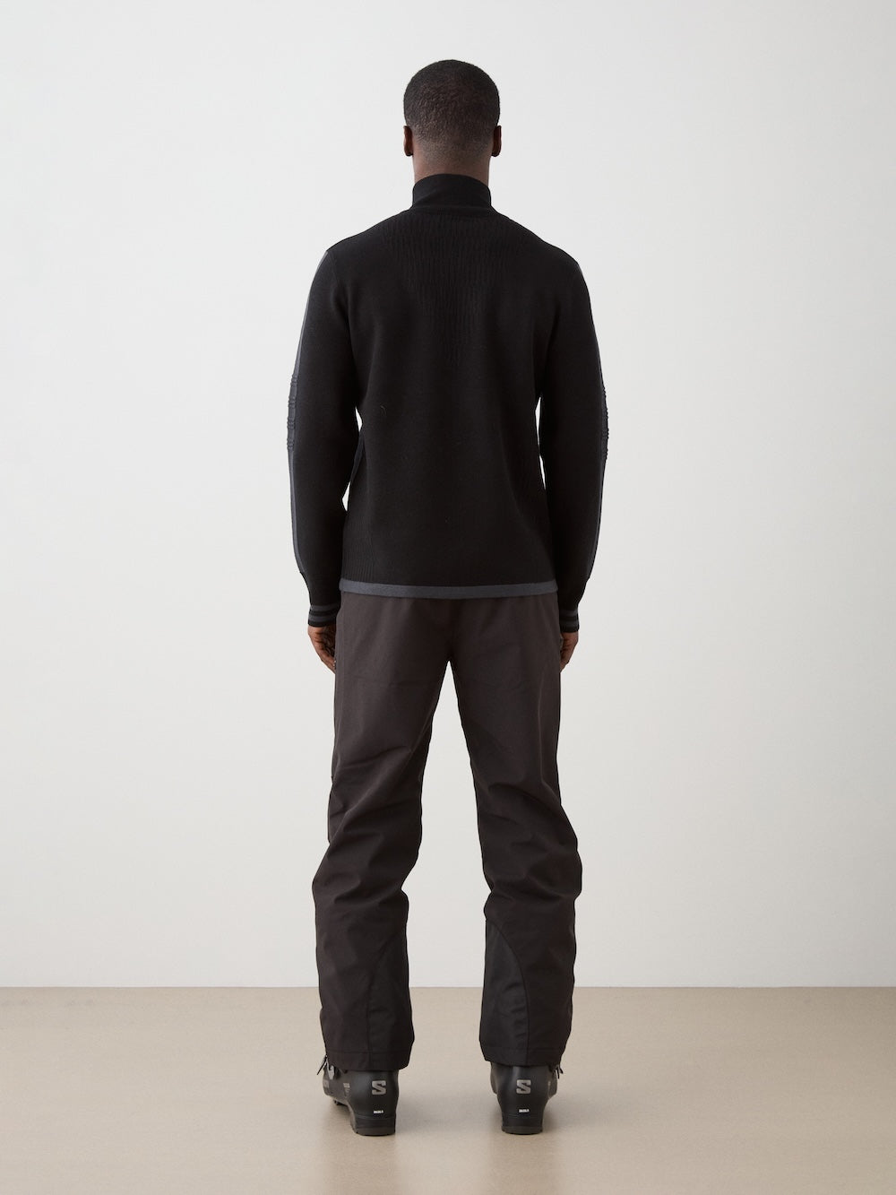 We Norwegians | FW25 | Mens Rocky Full ZipUp_Black | Model wearing this fine knitted sweater with a 2-way front zipper opening, designed in a retro style with subtle color blocks on the chest and sleeves - paired with black ski pants | Shot against an off-white background | Back