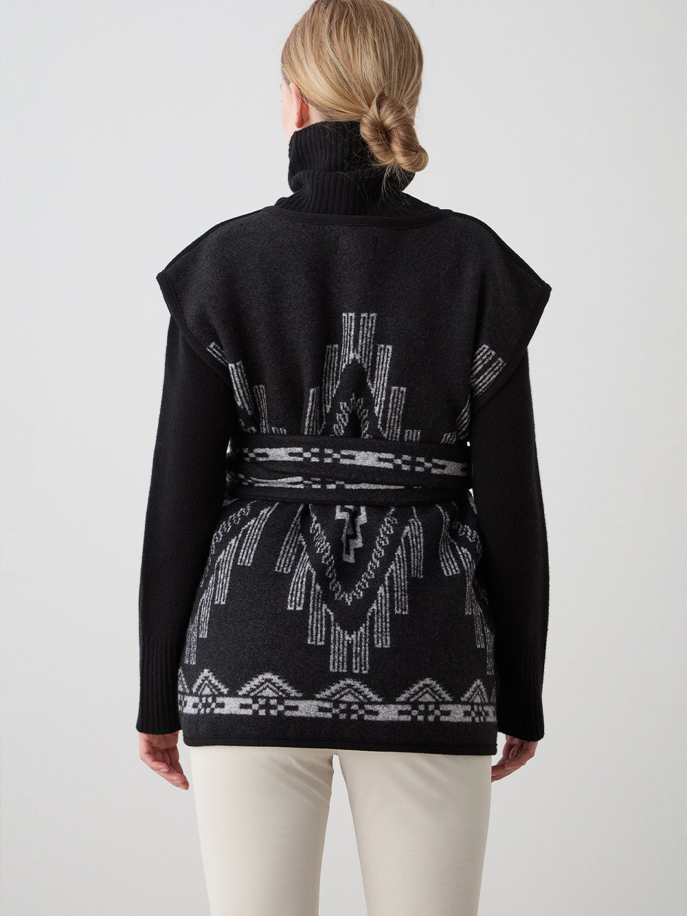 We Norwegians_FW25_Womens | Model is wearing the Pioneer vest | Black in color with a jacquard pattern | Vest has a matching belt to cinch the waist | Back view on a white background
