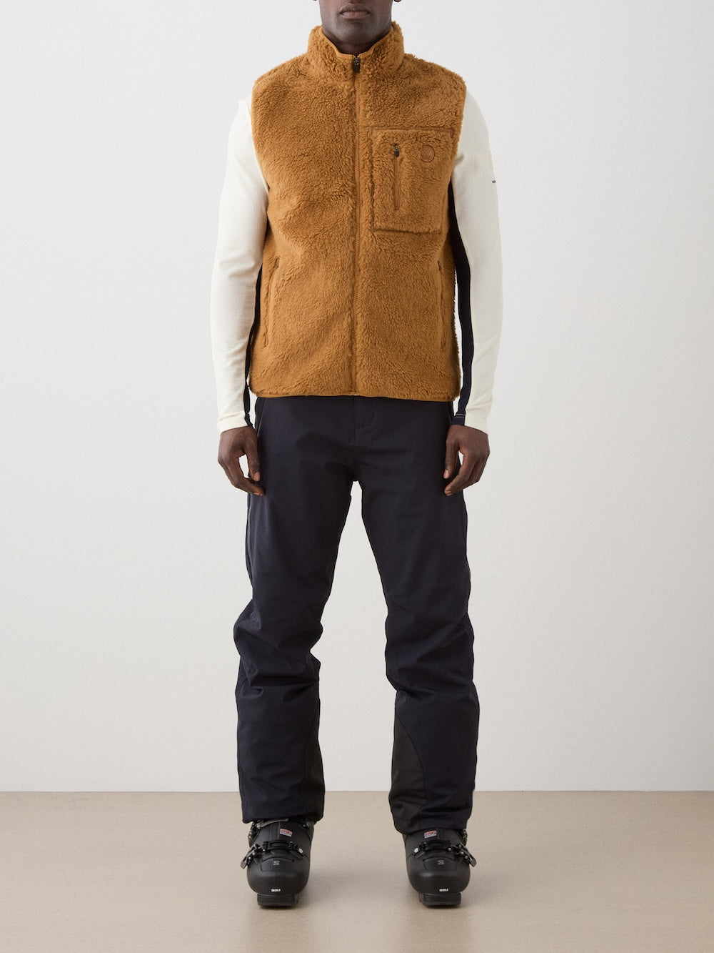 We Norwegians | FW25 | Mens Kebnekaise Vest_Cinnamon | Model wearing this fleece vest with front zipper opening, zipped chest pocket and side pockets -over an off-white top - paired with black ski pants | Shot against an off-white background | Front
